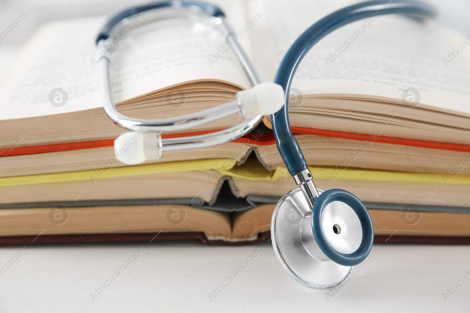 Photo of One new medical stethoscope and books on white wooden table, closeup