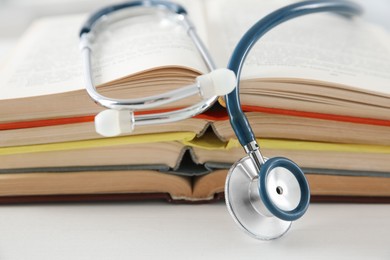 Photo of One new medical stethoscope and books on white wooden table, closeup