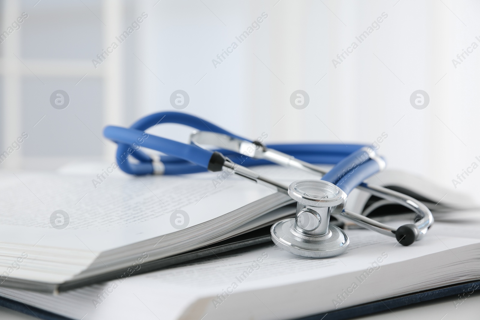 Photo of One medical stethoscope and books on white table, closeup