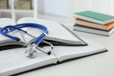 Photo of One medical stethoscope and books on white table, closeup