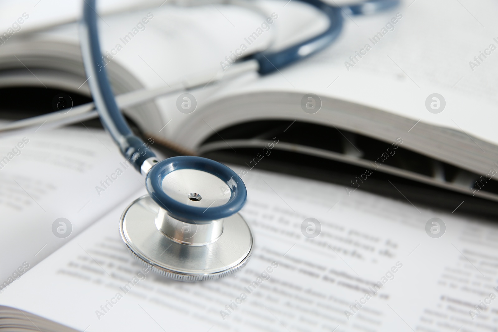 Photo of One medical stethoscope and books on table, closeup