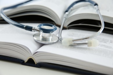 Photo of One medical stethoscope and books on white table, closeup