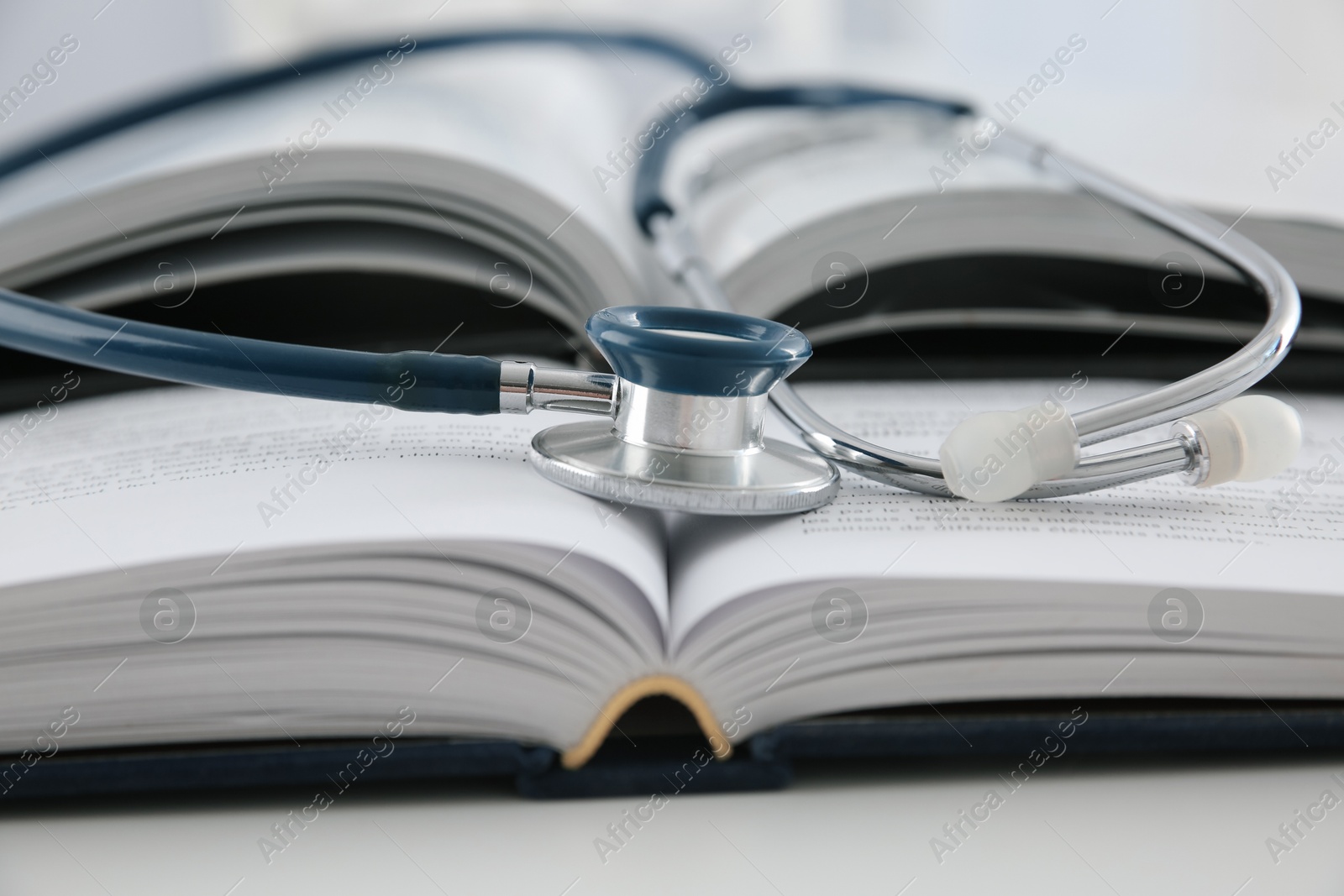 Photo of One medical stethoscope and books on white table, closeup