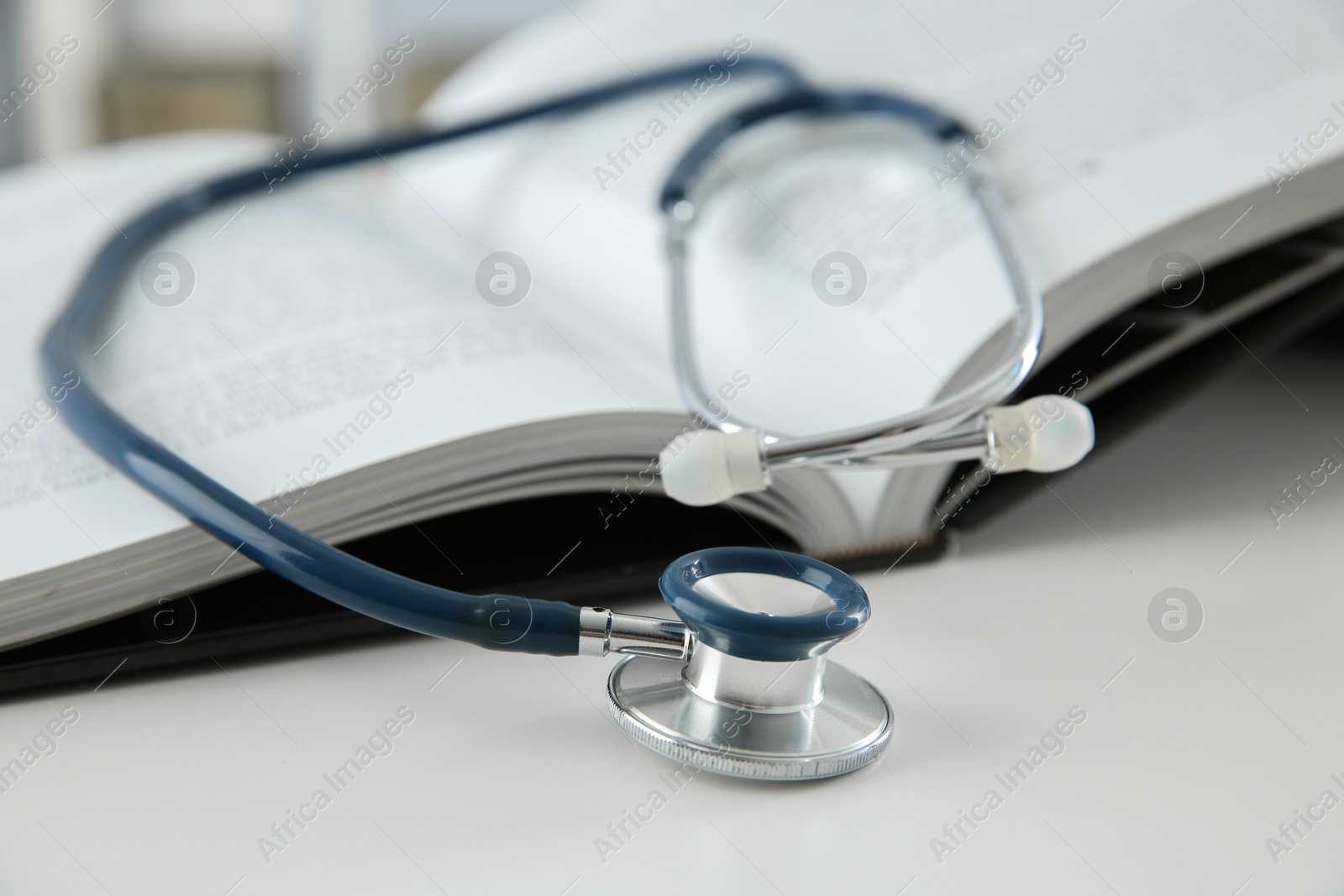 Photo of One medical stethoscope and book on white table, closeup