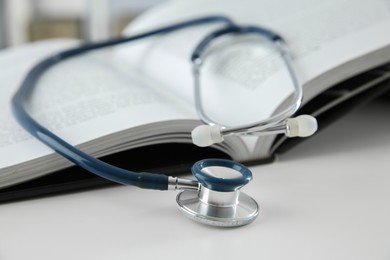 Photo of One medical stethoscope and book on white table, closeup