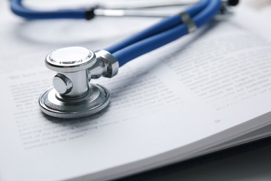 Photo of One medical stethoscope and book on table, closeup