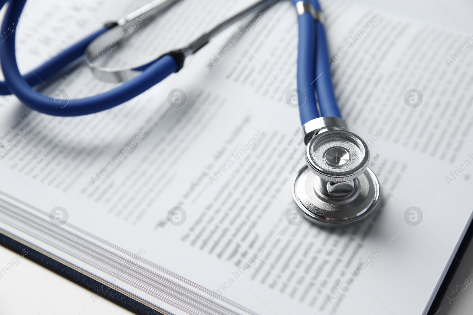 Photo of One medical stethoscope and book on table, closeup