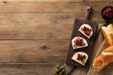 Delicious bruschettas with ricotta cheese, sun dried tomatoes and olives on wooden table, flat lay. Space for text