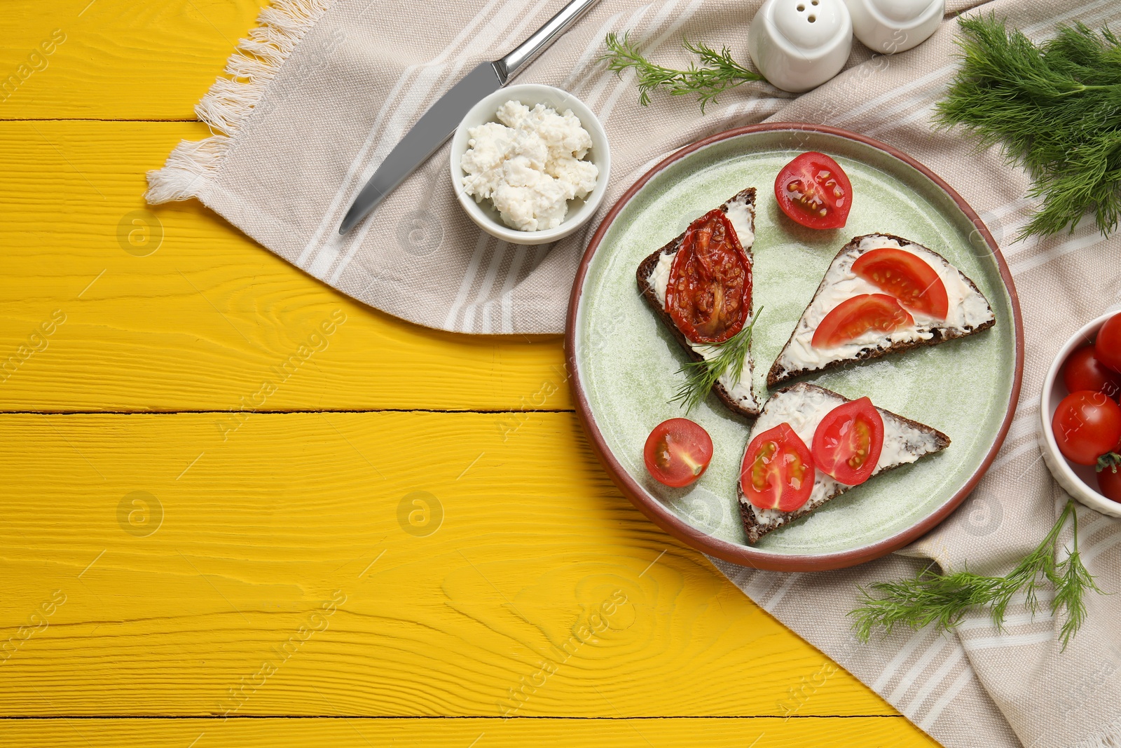 Photo of Delicious bruschettas with ricotta cheese, dill, fresh and sun dried tomatoes on yellow wooden table, top view. Space for text