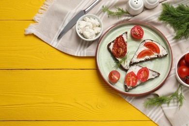 Delicious bruschettas with ricotta cheese, dill, fresh and sun dried tomatoes on yellow wooden table, top view. Space for text