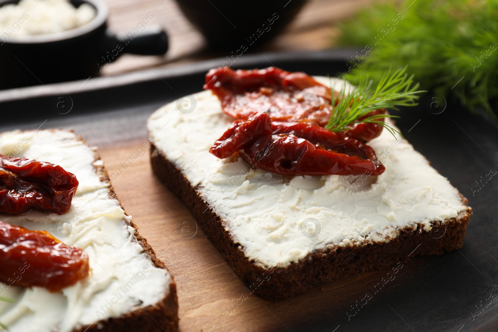 Photo of Delicious bruschettas with ricotta cheese, sun dried tomatoes and dill on wooden board, closeup