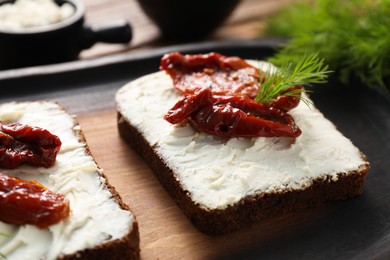 Delicious bruschettas with ricotta cheese, sun dried tomatoes and dill on wooden board, closeup