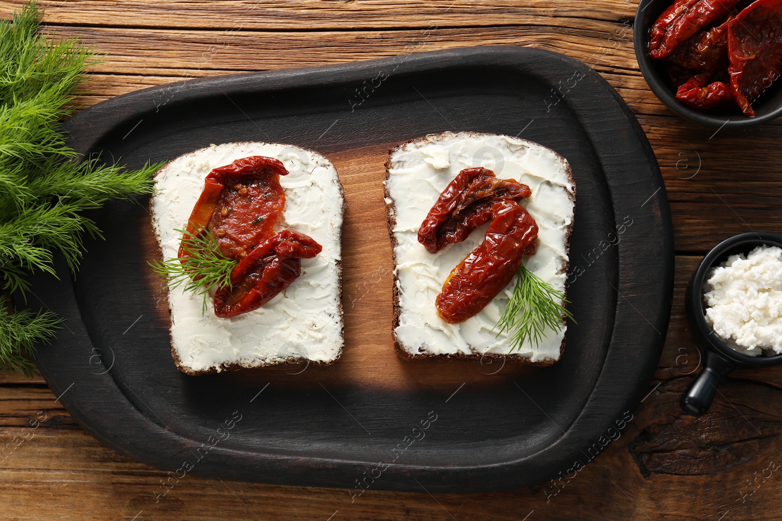 Photo of Delicious bruschettas with ricotta cheese, sun dried tomatoes and dill on wooden table, flat lay