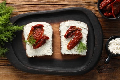 Delicious bruschettas with ricotta cheese, sun dried tomatoes and dill on wooden table, flat lay