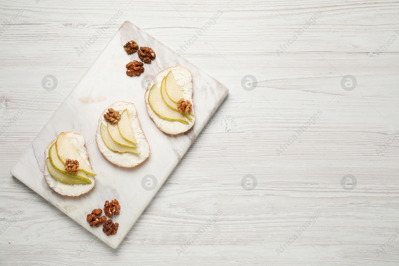 Photo of Delicious bruschettas with ricotta cheese, pears and walnuts on white wooden table, top view. Space for text