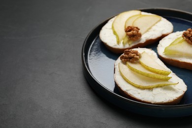 Delicious bruschettas with ricotta cheese, pears and walnuts on dark textured table, closeup. Space for text