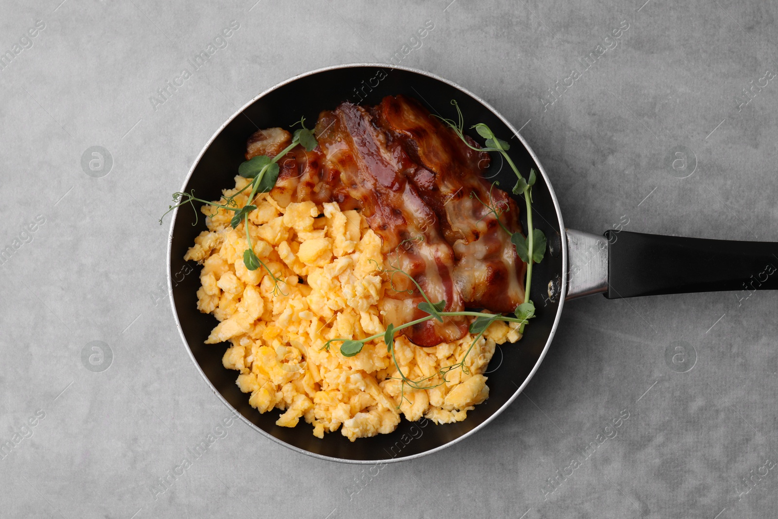 Photo of Delicious scrambled eggs with bacon in frying pan on grey table, top view