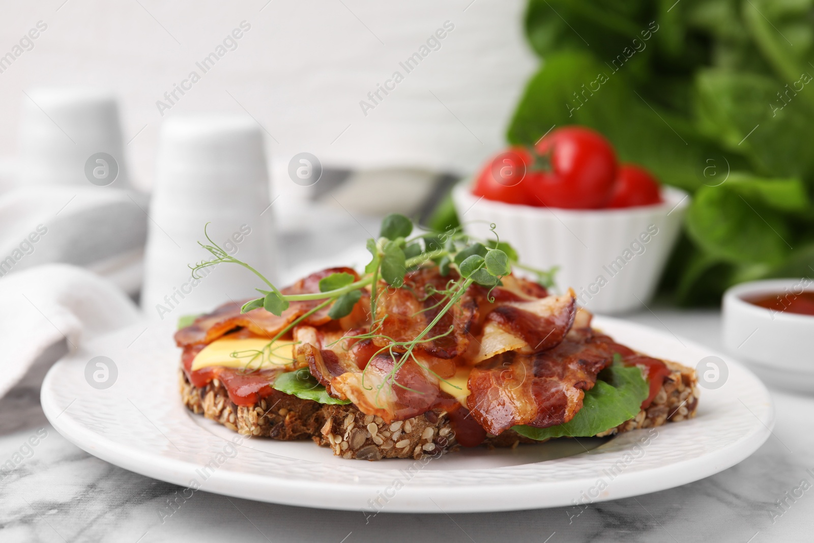 Photo of Tasty sandwich with bacon and microgreens on white marble table, closeup