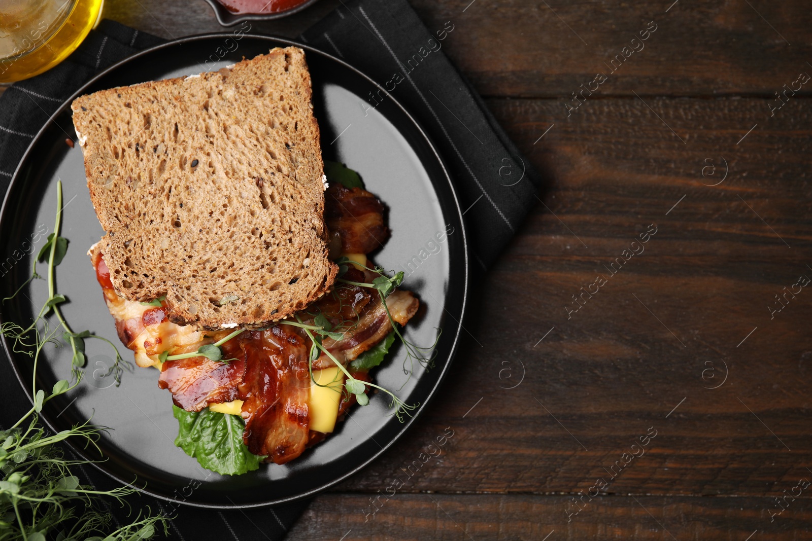 Photo of Tasty sandwich with bacon and microgreens on wooden table, flat lay. Space for text