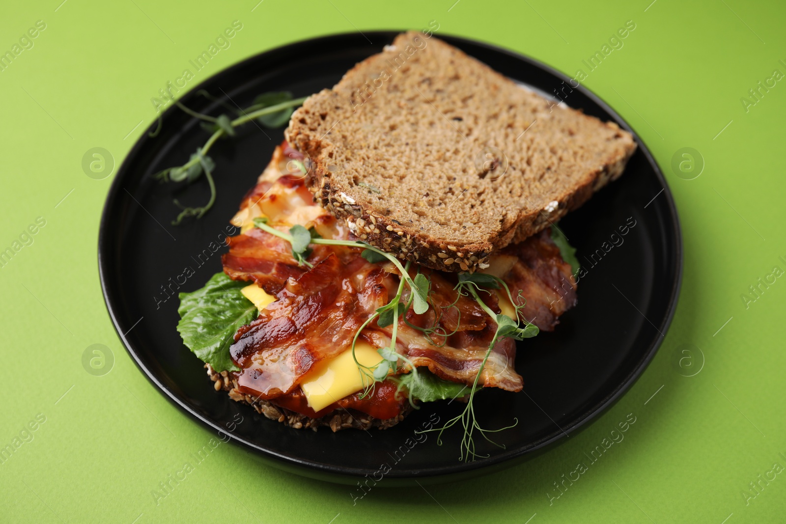 Photo of Tasty sandwich with bacon and microgreens on green table