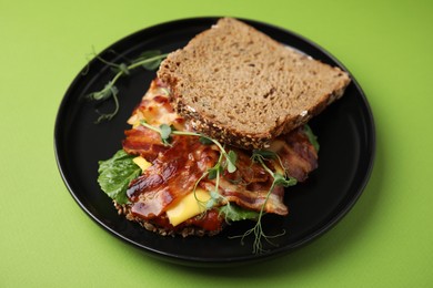 Photo of Tasty sandwich with bacon and microgreens on green table