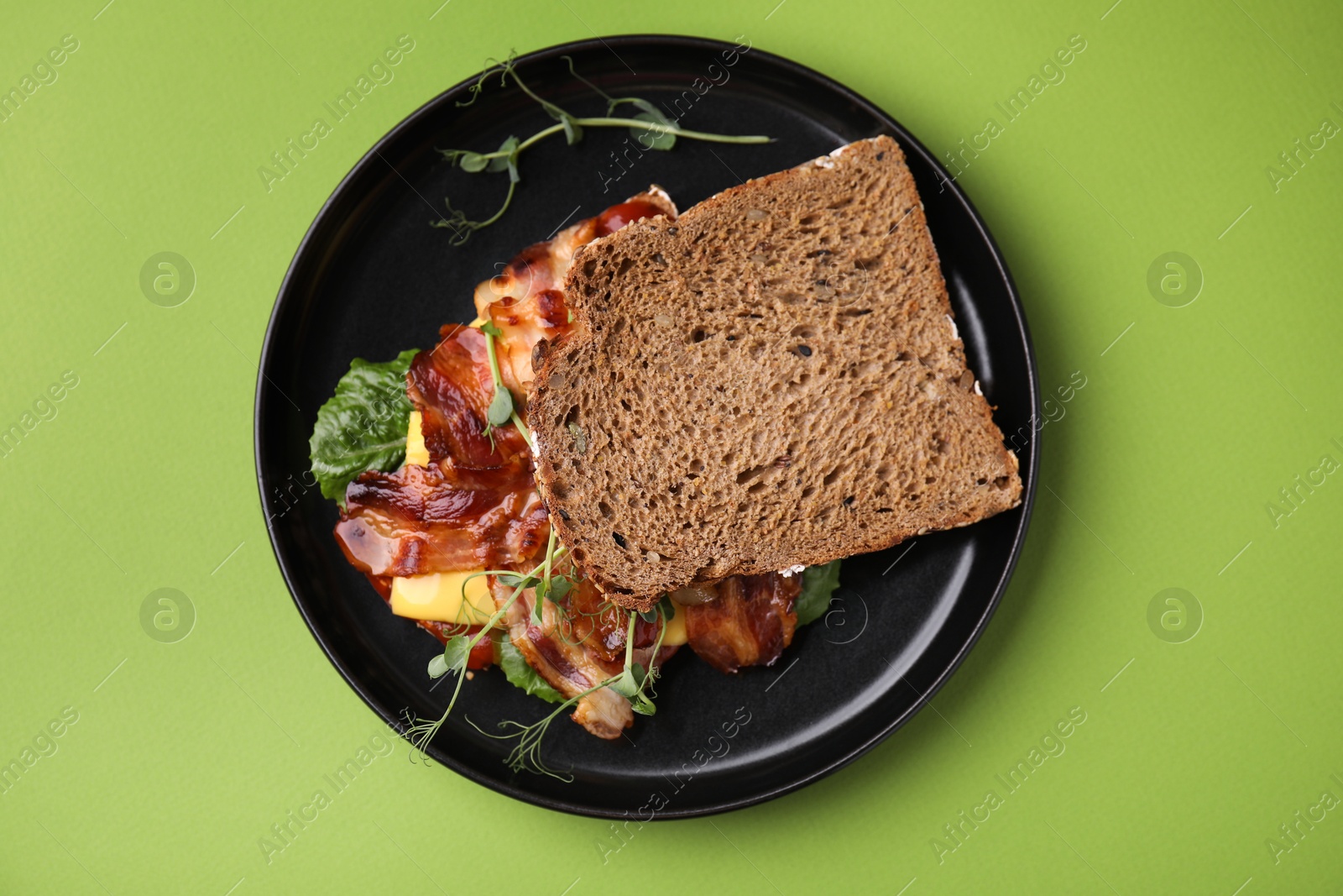 Photo of Tasty sandwich with bacon and microgreens on green table, top view