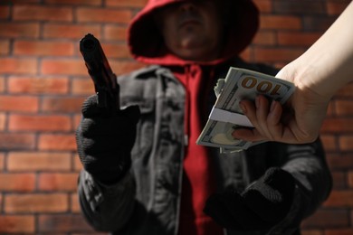 Photo of Woman giving money to criminal with gun near brick wall, closeup. Armed robbery