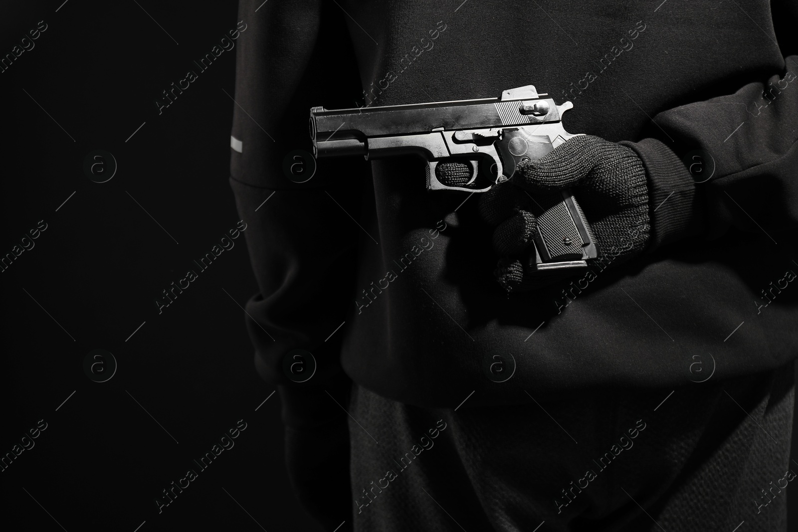 Photo of Man hiding gun behind his back on black background, closeup. Armed robbery