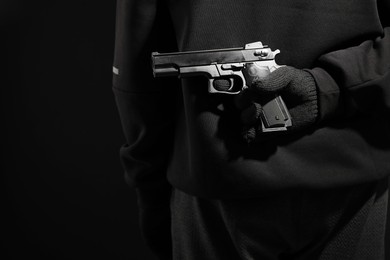 Man hiding gun behind his back on black background, closeup. Armed robbery