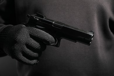 Dangerous criminal with gun on black background, closeup. Armed robbery