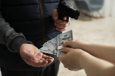 Photo of Woman giving money to criminal with gun indoors, closeup. Armed robbery