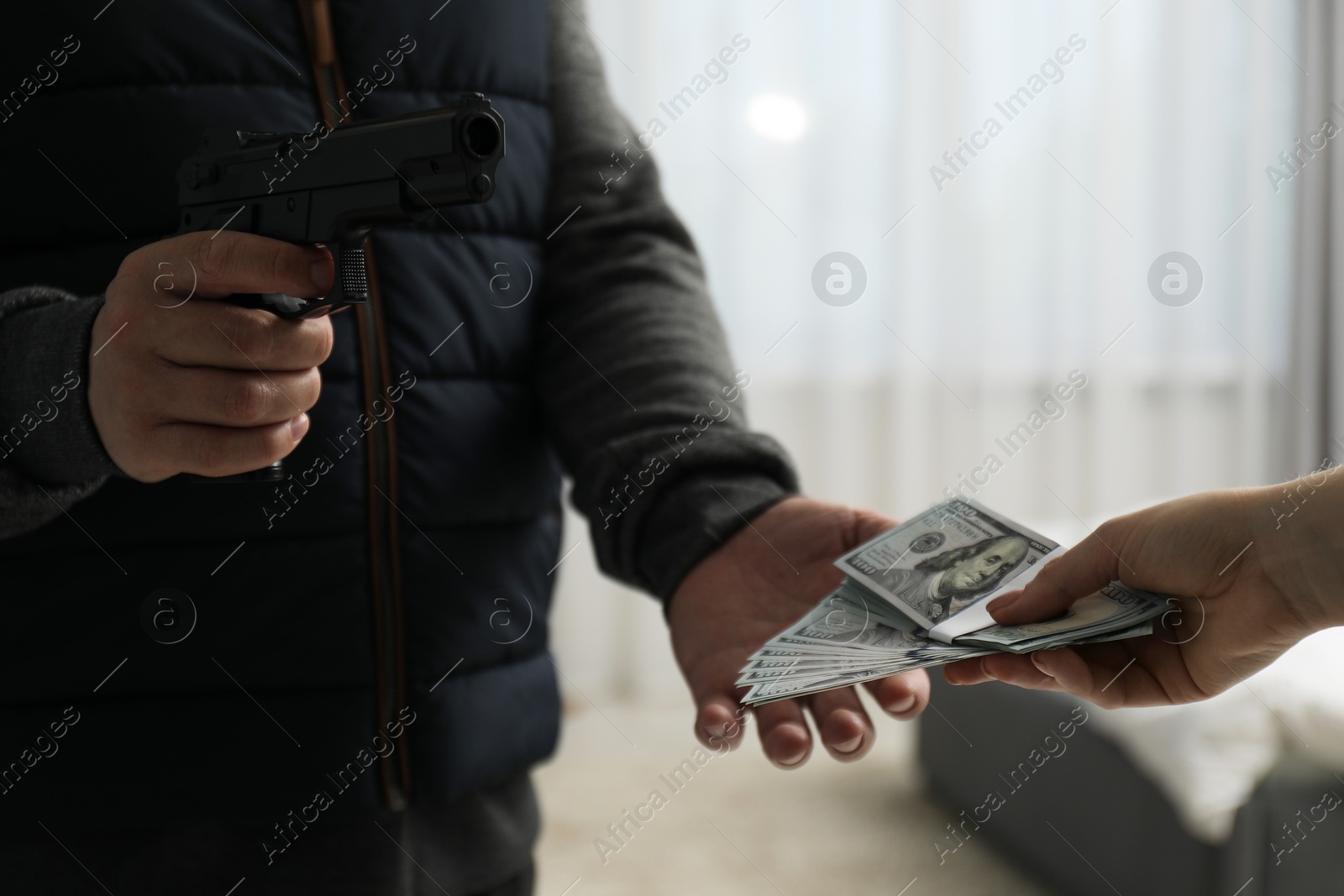 Photo of Woman giving money to criminal with gun indoors, closeup. Armed robbery