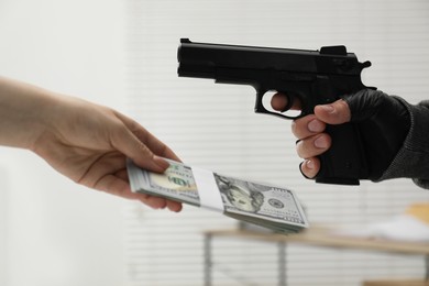 Woman giving money to criminal with gun indoors, closeup. Armed robbery