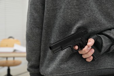 Photo of Man hiding gun behind his back indoors, closeup. Armed robbery