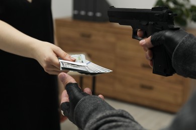 Photo of Woman giving money to criminal with gun indoors, closeup. Armed robbery