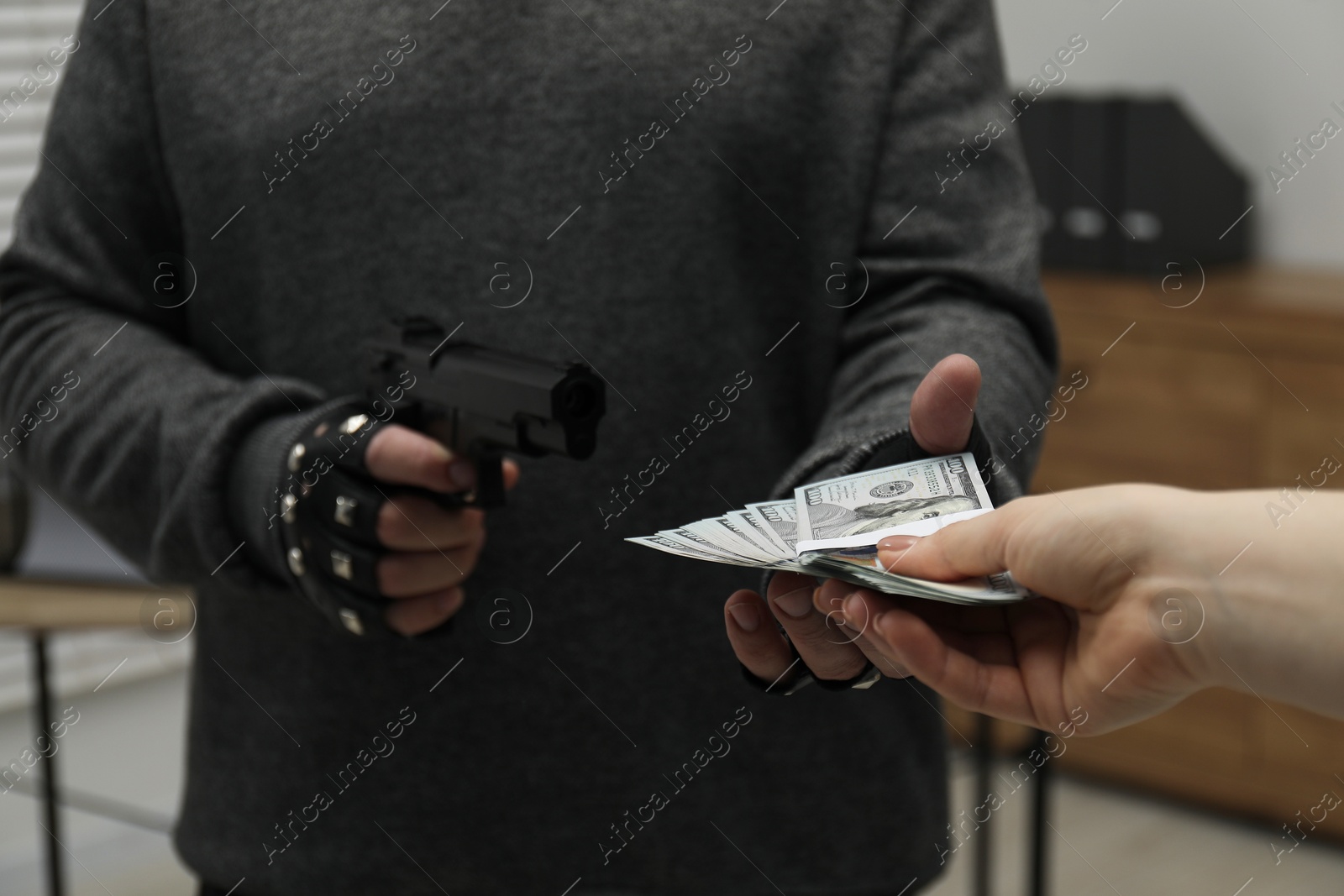 Photo of Woman giving money to criminal with gun indoors, closeup. Armed robbery