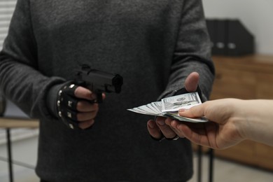 Woman giving money to criminal with gun indoors, closeup. Armed robbery