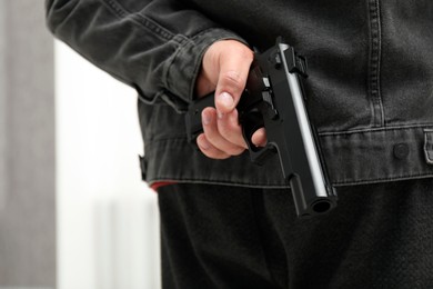 Photo of Man hiding gun behind his back indoors, closeup. Armed robbery