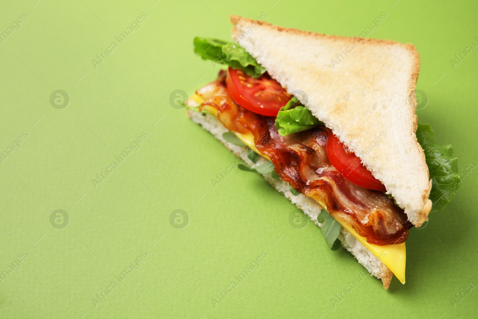 Photo of Delicious sandwich with fried bacon on green background, closeup. Space for text