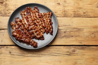 Photo of Slices of tasty fried bacon on wooden table, top view. Space for text