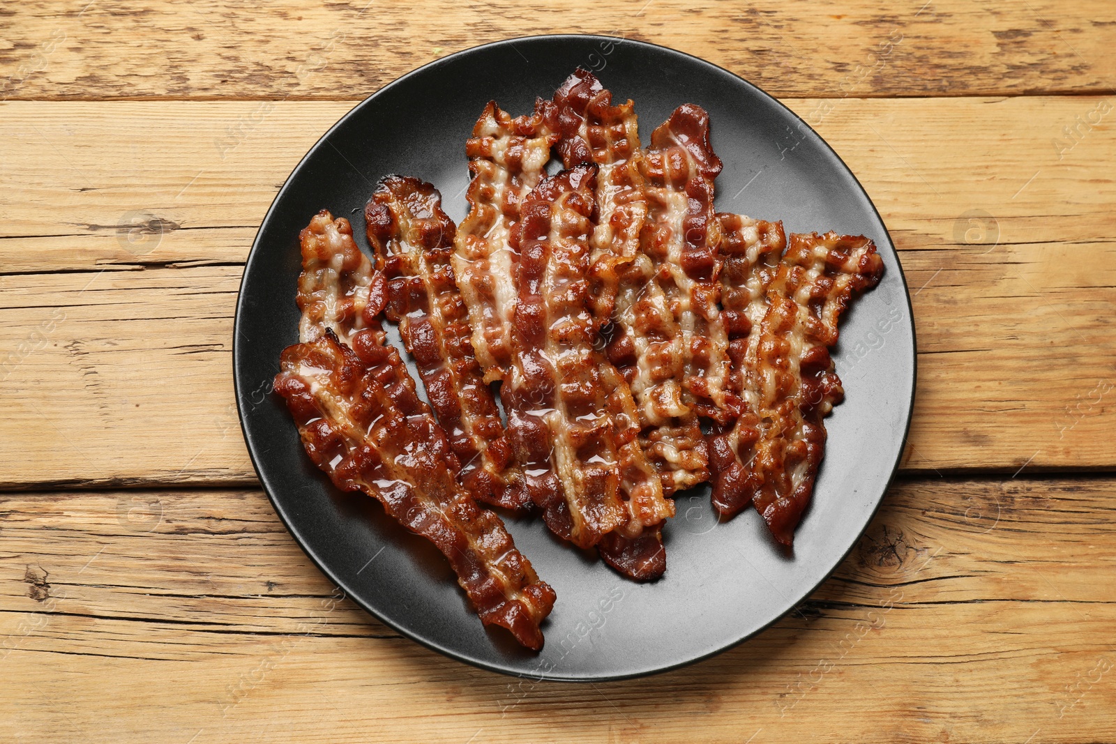 Photo of Slices of tasty fried bacon on wooden table, top view