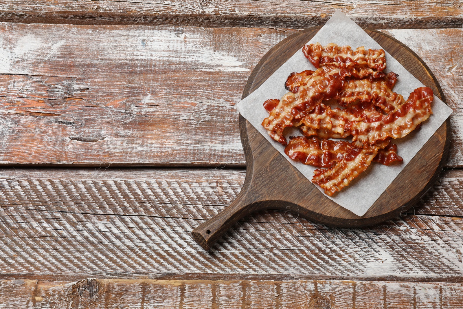 Photo of Slices of tasty fried bacon on wooden table, top view. Space for text