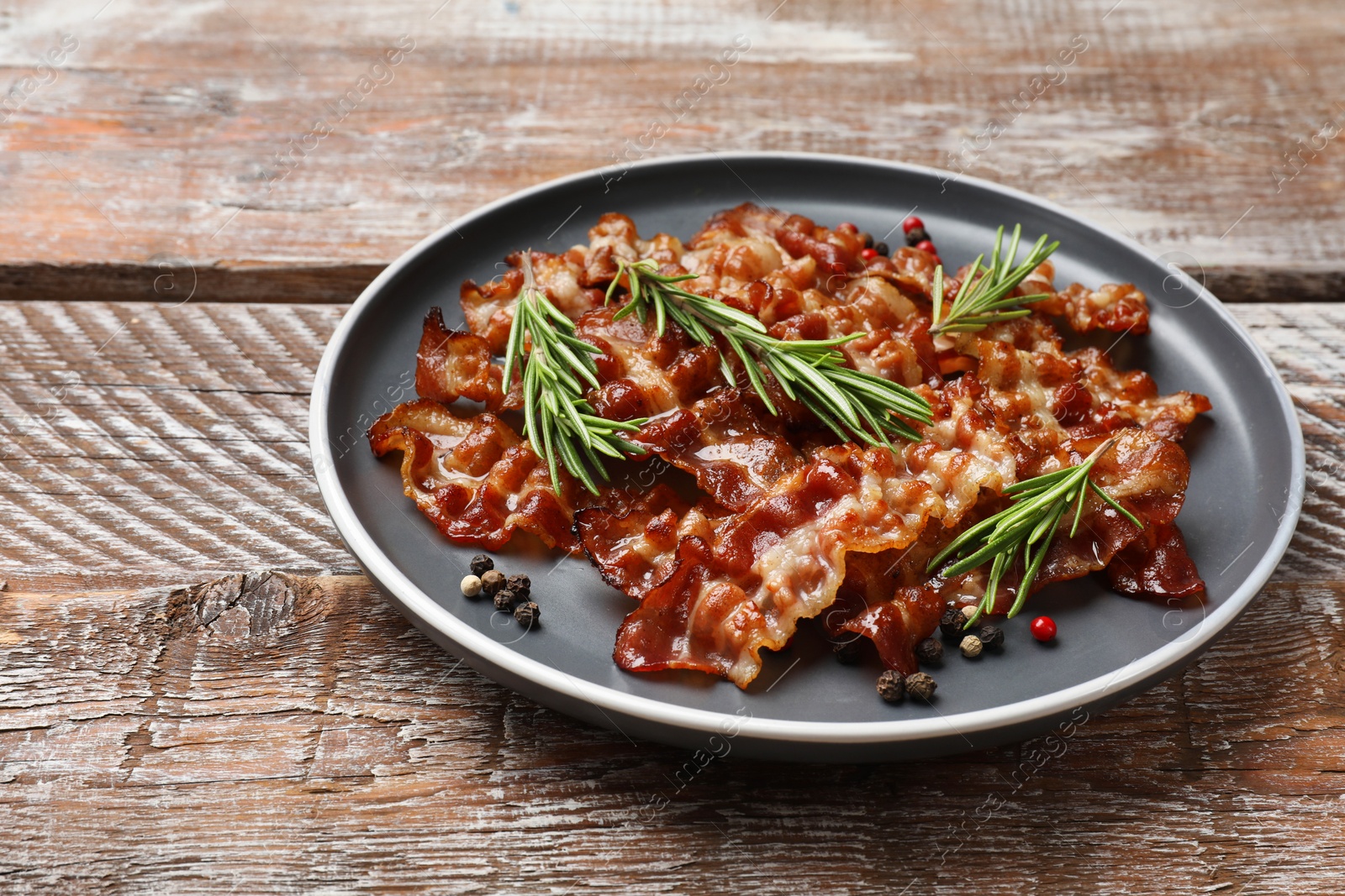 Photo of Slices of tasty fried bacon, peppercorns and rosemary on wooden table