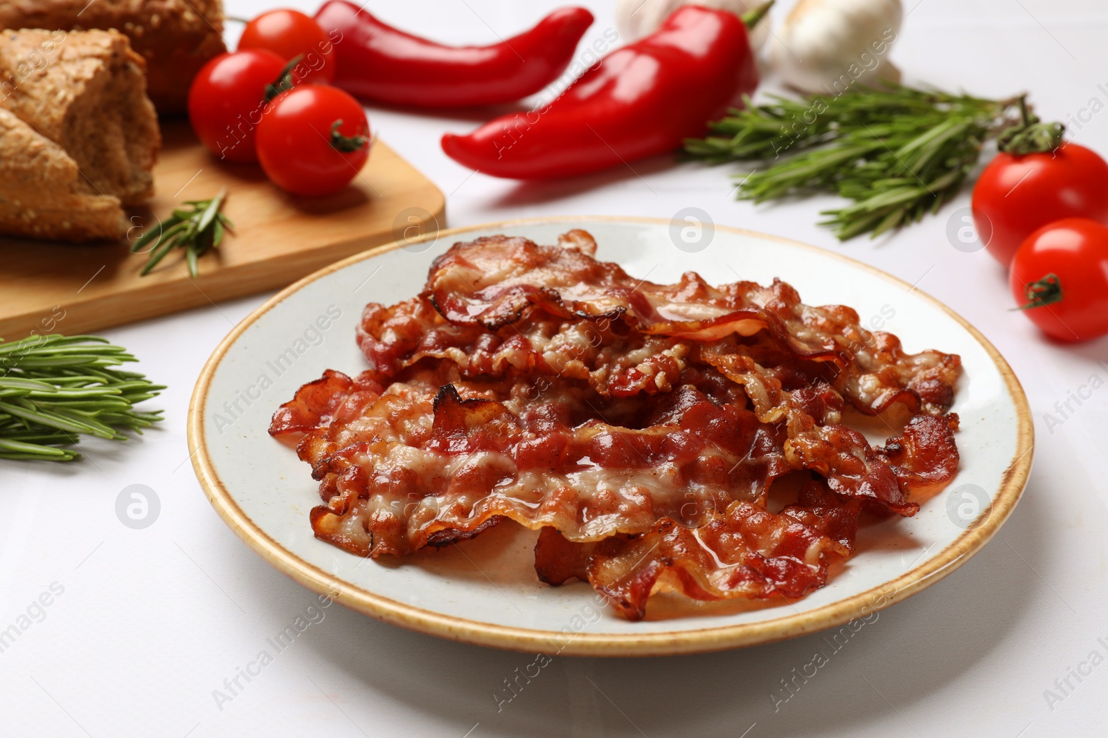 Photo of Slices of tasty fried bacon, tomatoes, different spices and bread on white table