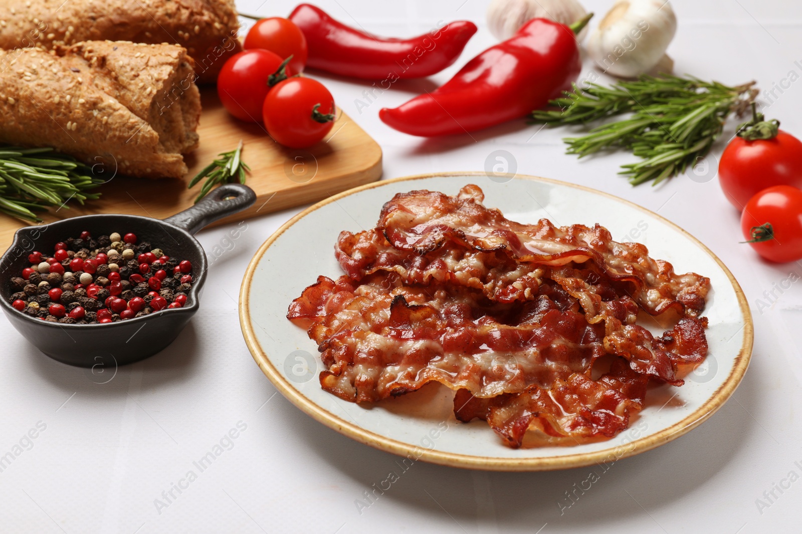 Photo of Slices of tasty fried bacon, tomatoes, different spices and bread on white table