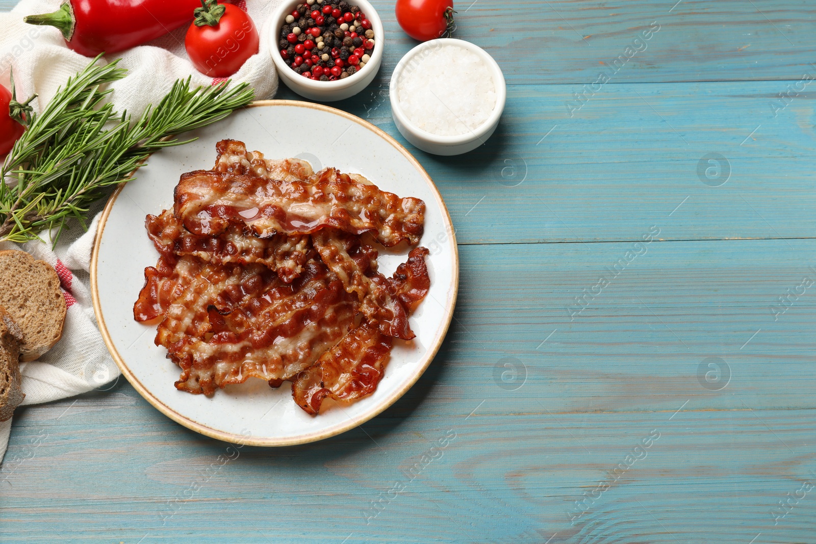 Photo of Slices of tasty fried bacon, different spices and bread on light blue wooden table, top view. Space for text