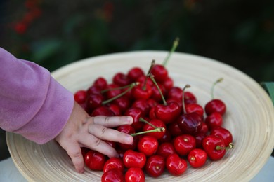 Photo of Child with plate of tasty red cherries outdoors, closeup