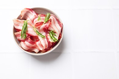 Photo of Slices of raw bacon and rosemary in bowl on white tiled table, top view. Space for text