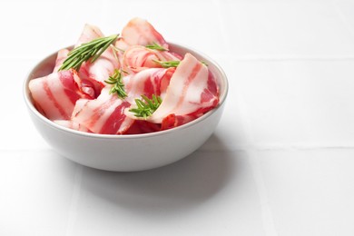 Photo of Slices of raw bacon and rosemary in bowl on white tiled table, space for text