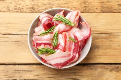 Photo of Slices of raw bacon and rosemary in bowl on wooden table, top view